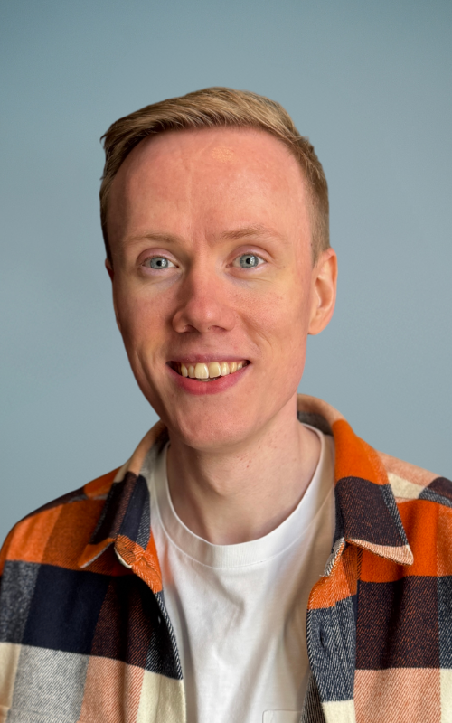 En ung person med kort blondt hår og blå øyne smiler til kameraet. De har på seg en hvit T-skjorte og en oransje, svart og hvit rutete flanellskjorte – perfekt stylet for presentasjoner på Cloud Native-teknologier. Bakgrunnen er ensfarget og lyseblå.